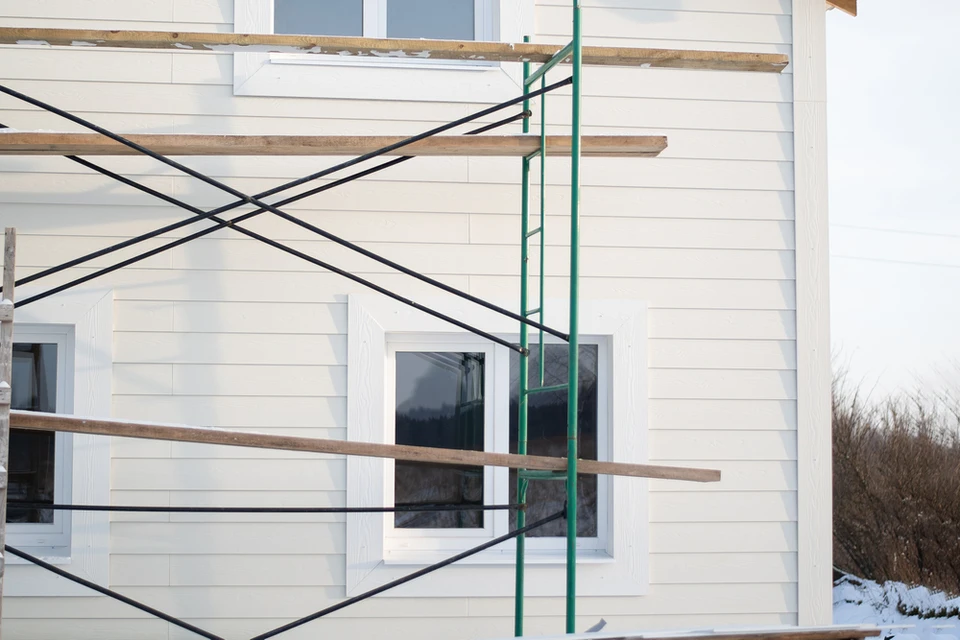 Chantier de construction résidentielle en cours, façade de maison avec échafaudage vert, ouvriers absents, environnement extérieur hivernal avec neige