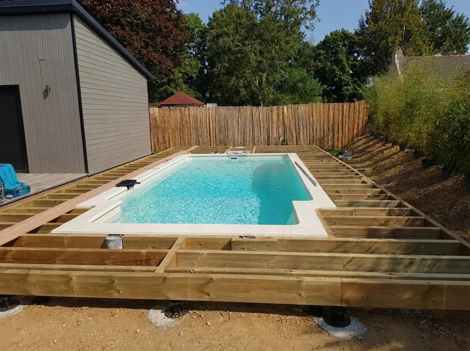Chantier de terrasse en bois autour d'une piscine coque polyester rectangulaire, installation en cours