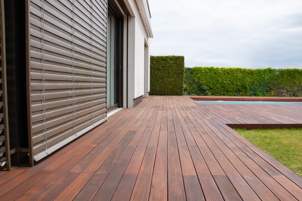 Photographie d'une terrasse en bois ou composite récemment construite, magnifiquement intégrée à l'architecture d'une maison résidentielle. La terrasse doit montrer des matériaux de qualité (bois clair ou composite naturel), une finition soignée, et un espace extérieur accueillant et fonctionnel prêt à la vie. La terrasse peut être partiellement meublée ou vide pour mettre en avant sa qualité constructive. Lumière naturelle mettant en valeur les matériaux et la réalisation. Pas de outils visibles, pas de chantier en cours.