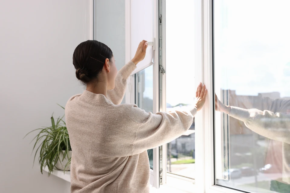 Installateur professionnel en casquette effectuant la pose d'une fenêtre PVC blanche à double vitrage dans un intérieur résidentiel